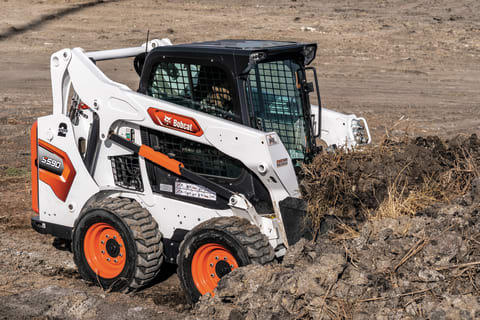 Operator Using Bobcat S590 Skid-Steer Loader With Bucket Attachment To Pile Dirt On Construction SiteOperator Using Bobcat S590 Skid-Steer Loader With Bucket Attachment To Pile Dirt On Construction Site