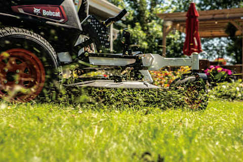 Grass Clippings Fly Past a Bobcat ZT6100 Zero-Turn Mower as It Mows a Residential Lawn 