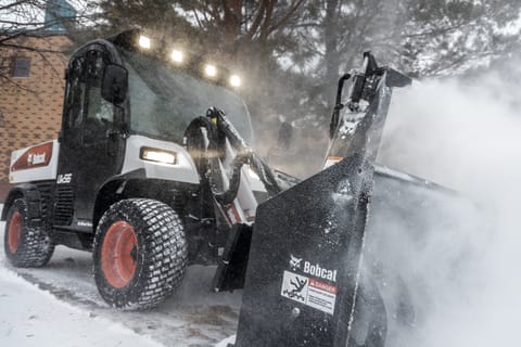 Operator Using UW56 Toolcat Utility Work Machine With Snowblower Attachment To Clear Sidewalk