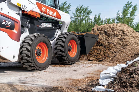 Operator Using Bobcat S76 Skid-Steer Loader With Bucket Attachment Moving Dirt