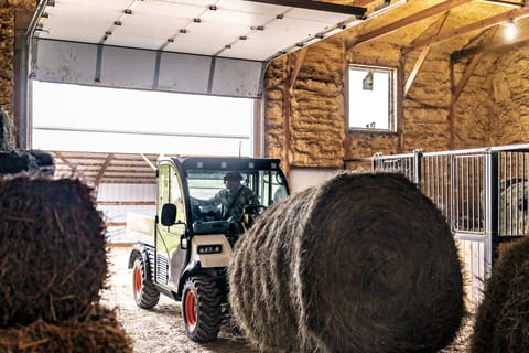 A Toolcat Utility Work Machine Grabbing Hay Bales Inside a Shed.
