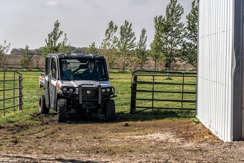 A Bobcat Utility Vehicle Driving Through a Fence Opening Toward a Metal Building.