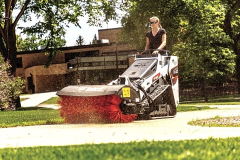 Groundskeeper Sweeps Sidewalk With Bobcat MtT100 Mini Track Loader With Angle Broom Attachment