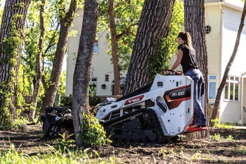 Woman operating an MT100 loader in-between two trees.