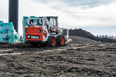 Bobcat S590 skid steer equipped with a pallet fork traveling on a construction site.
