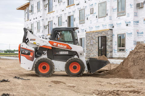 A Bobcat S76 Skid-Steer Loader Scoops Dirt From a Pile on an Apartment Building Construction Site