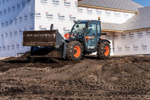 Bobcat TL619 Telehandler On A Construction Site Leveling Dirt Using The Combination Bucket.