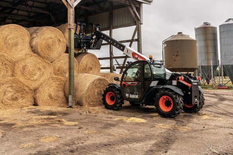 A Bobcat Telehandler Stacks Round Hay Bales on a Farm 