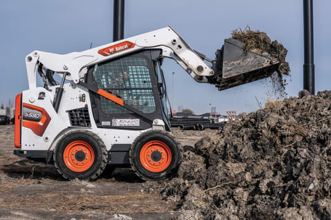 Operator Using Bobcat S590 Skid-Steer Loader With Bucket Attachment To Lift Dirt On Construction Site