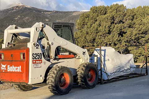 Bobcat S250 skid-steer hauling snowmobile in front of mountains