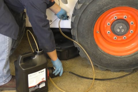 A Bobcat technician pumping new fluid into the chaincase.