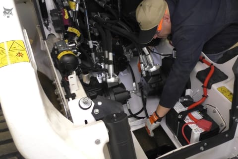 Technician routing the hydraulic drain hose on a Bobcat R-Series loader.