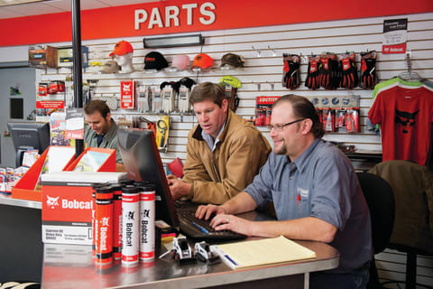 Bobcat customer service expert looking up fluid analysis kits on computer, while customer looks on approvingly.