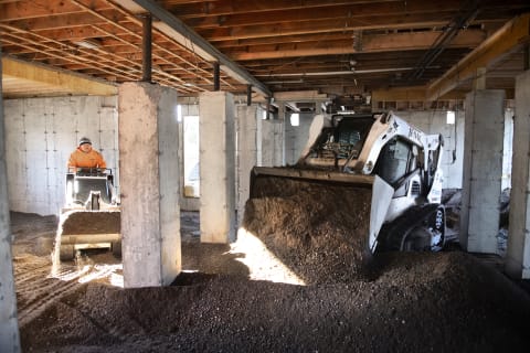 Operator Using A Bobcat T650 Compact Track Loader To Dump Soil In Building Foundation While A Second Operator Uses A Bobcat MT85 Mini Track Loader To Redistribute And Grade Dirt 