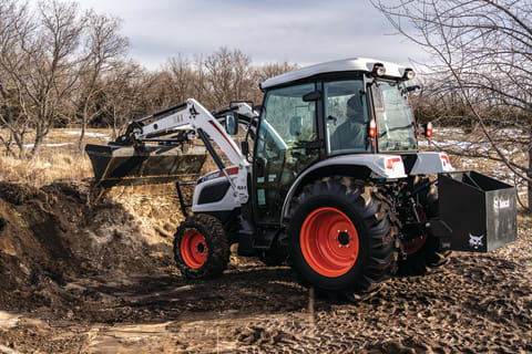 A Compact Tractor Dumping Material With a Bucket.