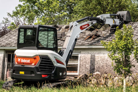 Operator Using Bobcat E60 Compact Excavator With Extendable Arm And Clamp Attachment To Demolish House
