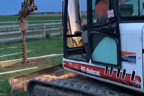 Operator Digging Post Holes With A Bobcat Compact Excavator And Auger Attachment.