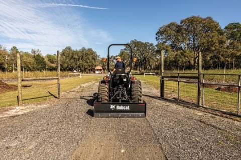 Bobcat CT2025 Compact Tractor With 3pt Box Blade Attachment Traveling Down Gravel Road