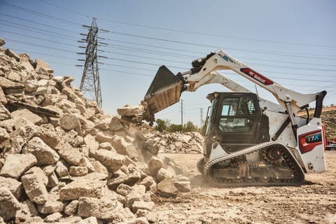 A Bobcat T7X All-Electric Compact Track Loader Dumping Rocks Into a Pile