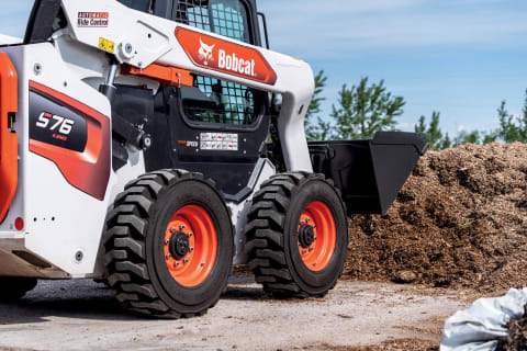 A Bobcat S76 Skid-Steer Loader With Standard-Duty Tires Approaches a Large Pile of Dirt
