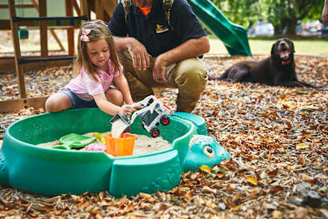 A Child Plays With a Bobcat Skid-Steer Loader Toy in a Sandbox