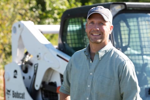 Chase Burns, owner of Dogwood Land Management, standing in front of his Bobcat loader.