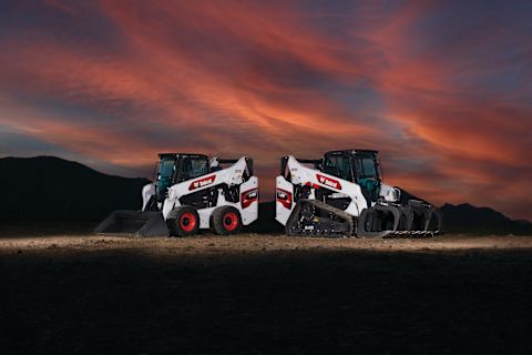 Bobcat compact track loader and skid-steer loader parked back-to-back on jobsite with sunset