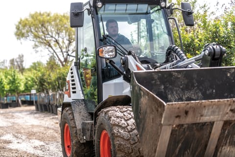 Bobcat Compact Wheel Loader Operator Sitting In Cab Driving Through Jobsite.