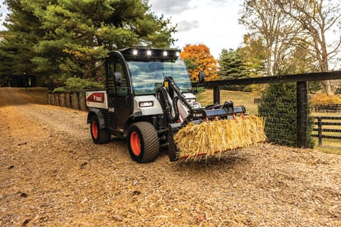 A Toolcat Utility Work Machine Carries a Hay Bale With a Grapple Attachment