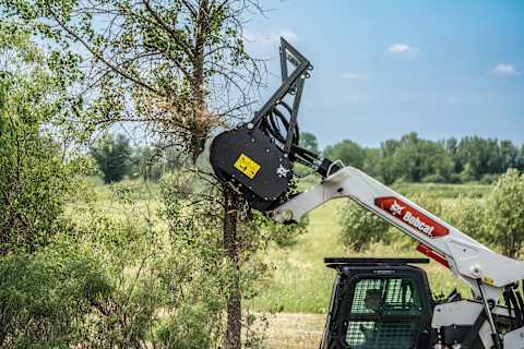 Bobcat T86 compact track loader powering forestry attachment while clearing trees.