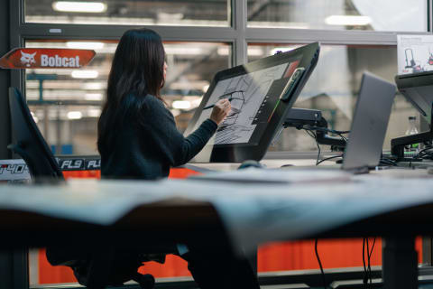 A Bobcat Designer Works on Sketches on a Screen at Her Desk