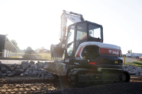 A Bobcat E85 mini excavator operated by Samron Midwest Contracting employee scoops concrete with bucket on jobsite. 