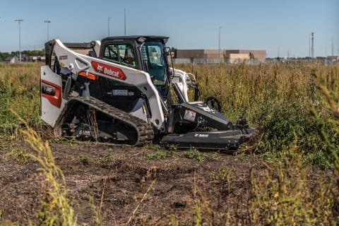 Bobcat compact track loader uses a Brushcat rotary cutter to chop down tall grass.