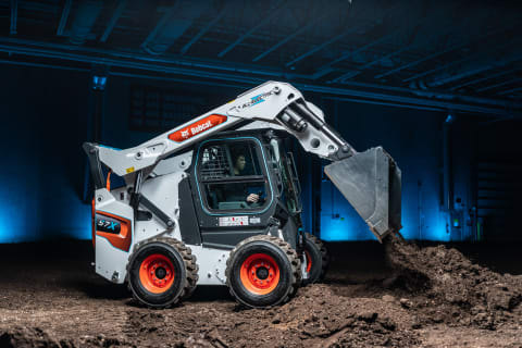 The all-electric Bobcat S7X skid-steer loader raises its lift arms to drop a bucket of dirt.