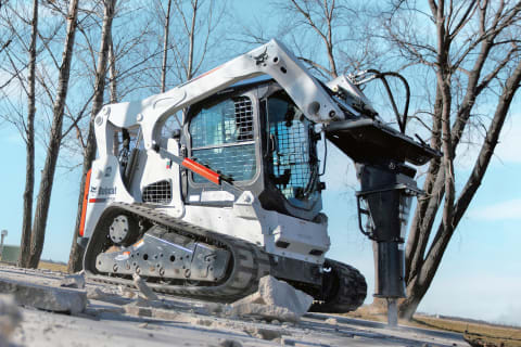 Un opérateur se sert d’une chargeuse compacte sur chenilles Bobcat équipée d'une marteau hydraulique pour briser du béton.