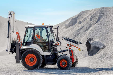 An operator using a Bobcat Compact Backhoe Loader to transport fine materials with the front bucket.