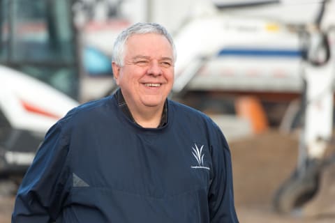 Rick Alischer, owner of Complete Site Services smiles with Bobcat Excavator behind him.