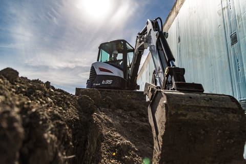 Bobcat E35 compact (mini) excavator and bucket attachment digging inside a trench