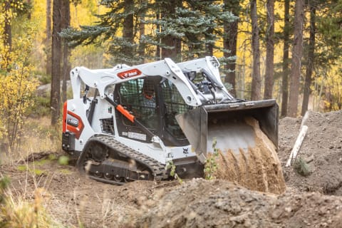 A Bobcat T595 Compact Track Loader Dumps Dirt in a Forest Clearing