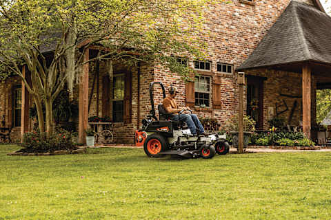 Homeowner mowing nicely manicured yard with the Bobcat ZT3500 zero-turn riding mower with brick home in the background