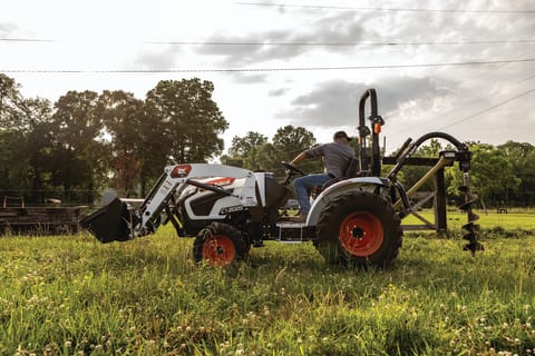 A Bobcat compact tractor drills a hole with the auger attachment.