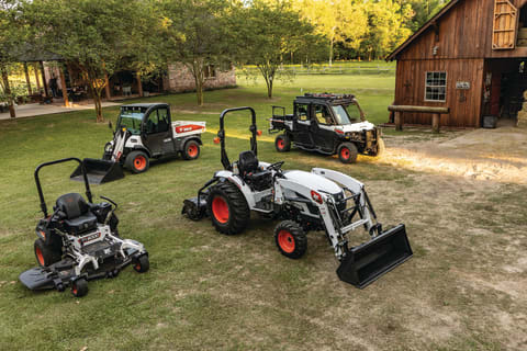 A Lineup of Bobcat Equipment Parked Near a Barn, Including a Bobcat Zero-Turn Mower, Toolcat Utility Work Machine, Bobcat Compact Tractor and Bobcat Utility Vehicle