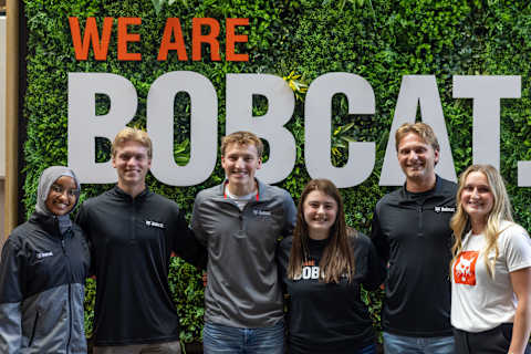 Student interns at luncheon posing in front of “We are Bobcat” sign.