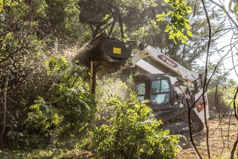 Bobcat T86 Compact Track Loader with Drum Mulcher Attachment Operating in Wooded Area