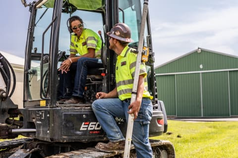 Jessie Hamilton Speaks With a Co-Worker From the Cab of a Bobcat E60 Compact Excavator 