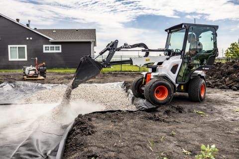 A Bobcat small articulated loader works on a landscaping project in a residential neighborhood