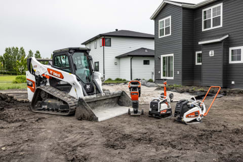 A Bobcat Compact Track Loader Parked on an Unplanted Residential Lawn Next to Several Bobcat Compaction Machines