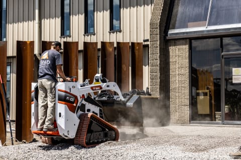 A Bobcat Mini Track Loader Operator Looks Down Toward the Bucket as He Dumps Material