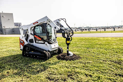 Bobcat T650 compact track loader with auger attachment drilling into soil on a jobsite