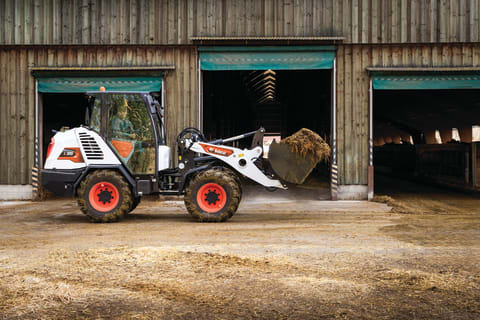 The Bobcat L95 Compact Wheel Loader Carries a Load of Hay at a Farmstead.